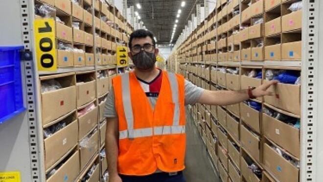 亚马逊员工Shams Hussamy站在他在安大略省工作的物流中心拍照。