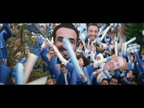 An image of a man holding a box with the Amazon Prime logo with a crowd of people wearing blue and white cheering him.