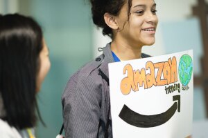 A girl holds up a sign that reads, "Amazon treding global" while another girl smiles and looks at her.