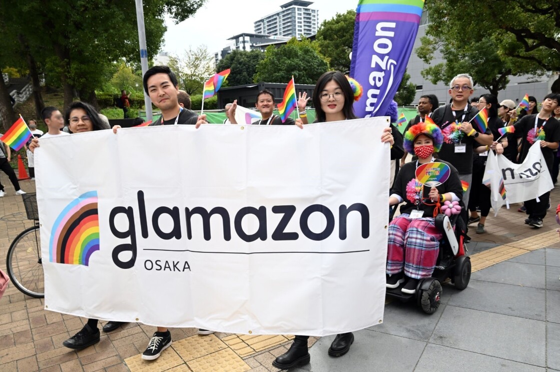 女性2人と男性1人はGlamazon Osakaと書かれた横断幕を持って、グループ最前列にいる。後ろには数人の人々が小さなレインボーフラッグを持って歩いている