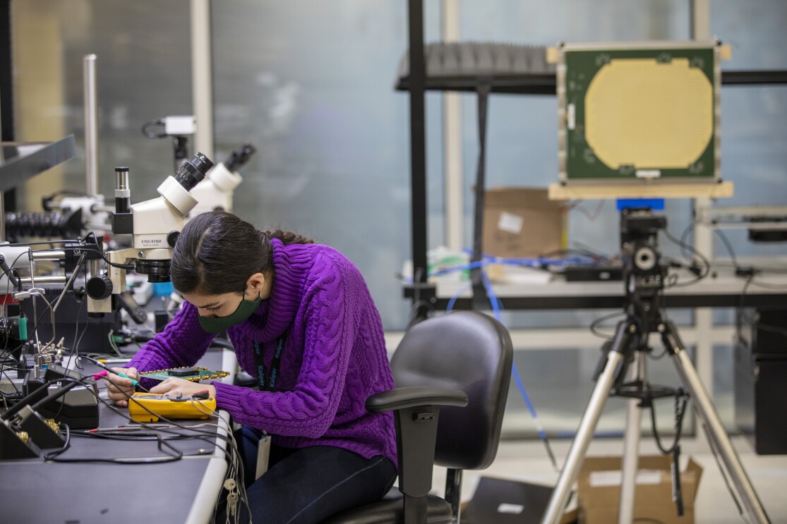 A woman sits at a table while working on an engineering project for Project Kuiper.