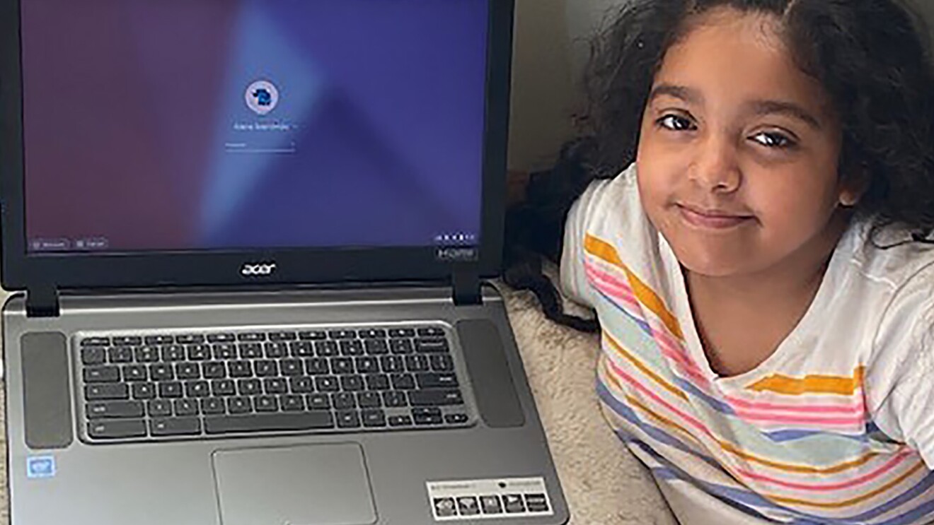 An elementary age student sits with their laptop computer in their home