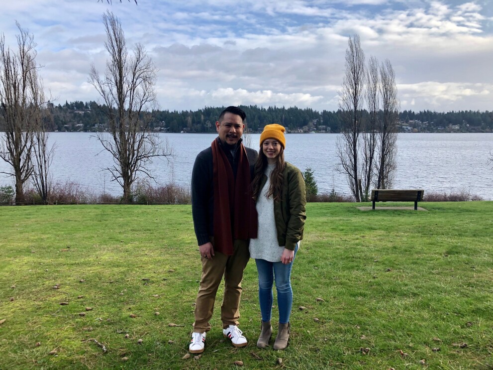 A woman and man sit on a bench in front of a lake.