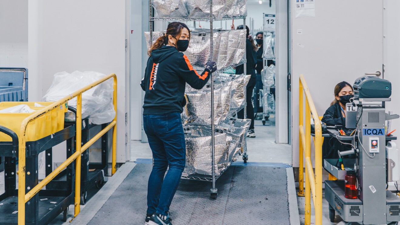 An employee wheeling a cart from the chiller filled at the Amazon Fresh fulfillment centre