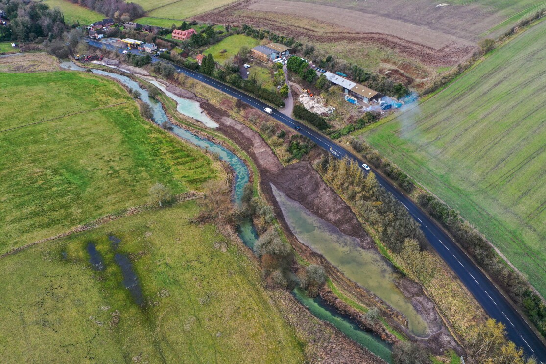 Aerial view of winding river alongside road and farmland