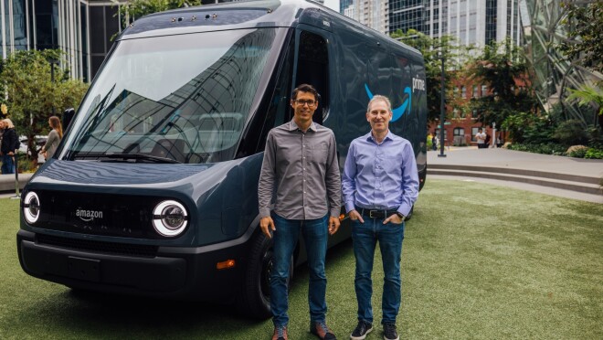 Andy Jassy and RJ Scaringe stand side-by-side in front of a Rivian Amazon delivery vehicle that is parked outside the Spheres at Amazon headquarters.