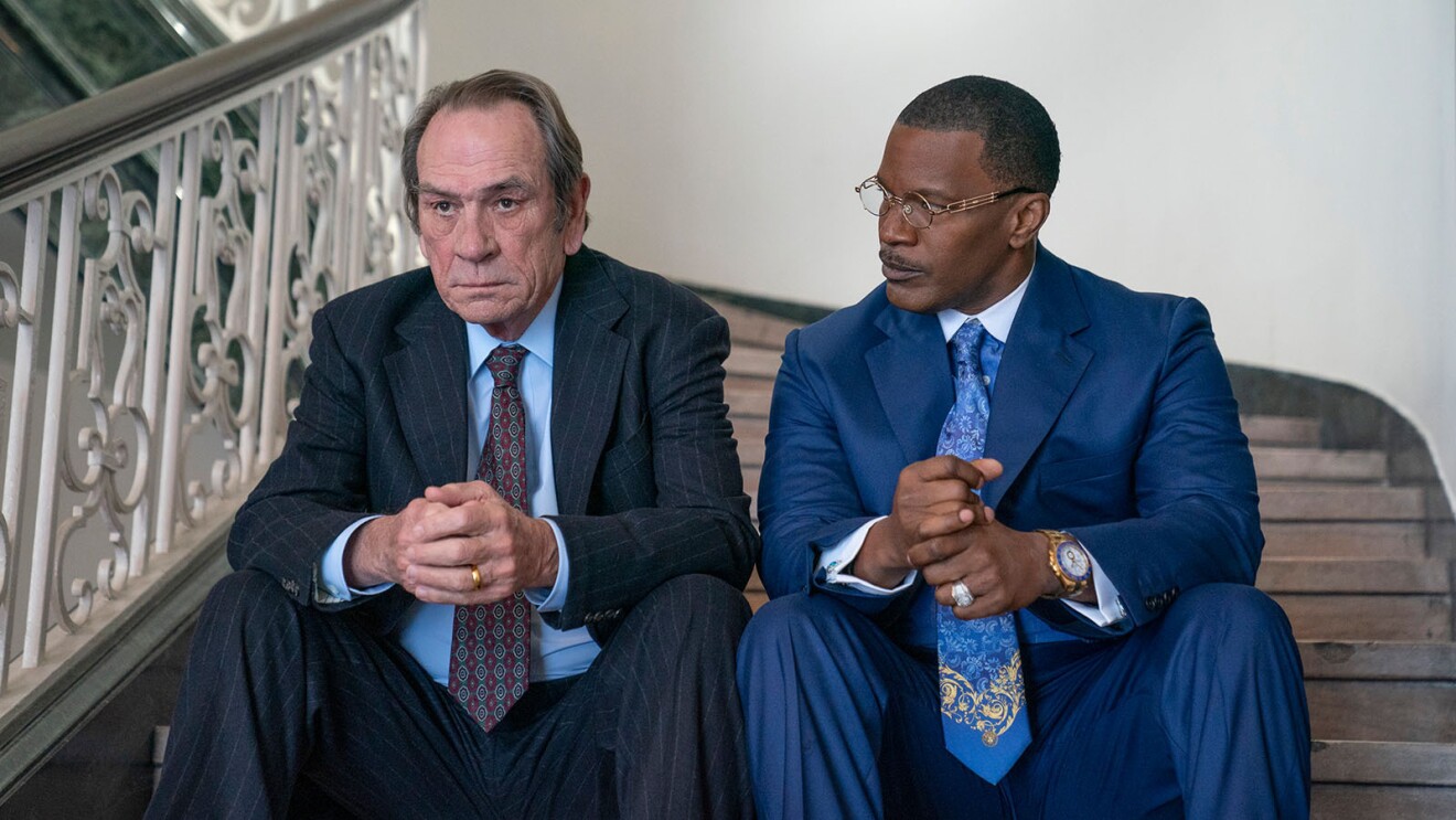 Tommy Lee Jones and Jamie Foxx sitting next to each other on a staircase in the movie, The Burial.