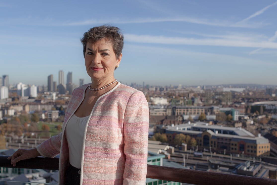 Christiana Figueres standing on a balcony overlooking a city skyline. 