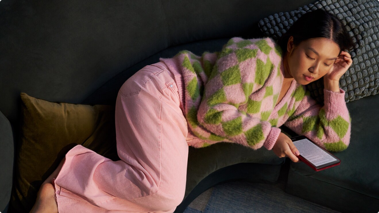 Woman lounging on couch reading e-book in cozy sweater
