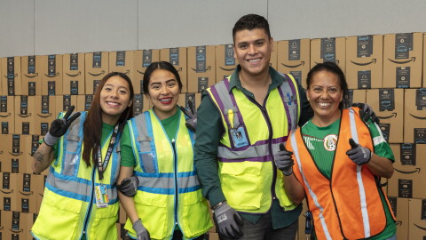 Cuatro trabajadores de Amazon posando delante de cajas de Amazon en un centro logístico.