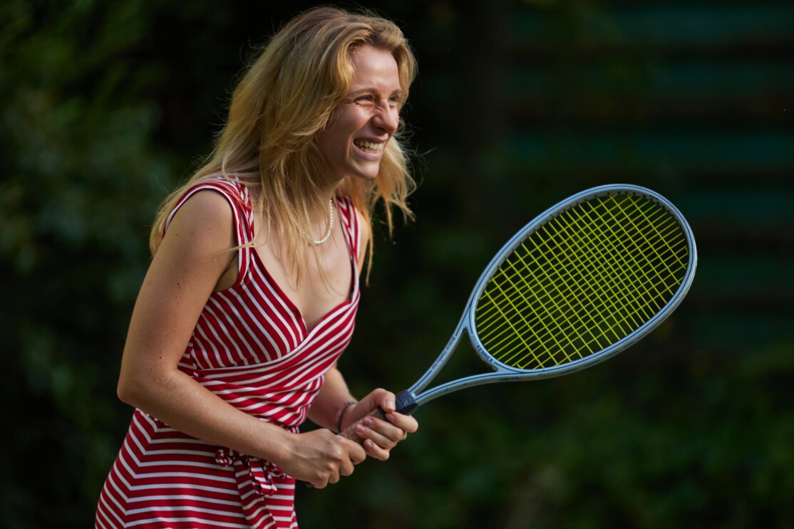 Szene aus Perfect Match, der Geschichte über Steffi Graf und Andre Agassi. Lena Klenke in der Rolle als Steffi Graf in einem rot-gestreifen Tenniskleid. Sie hält einen Tennisschläger in der Hand.