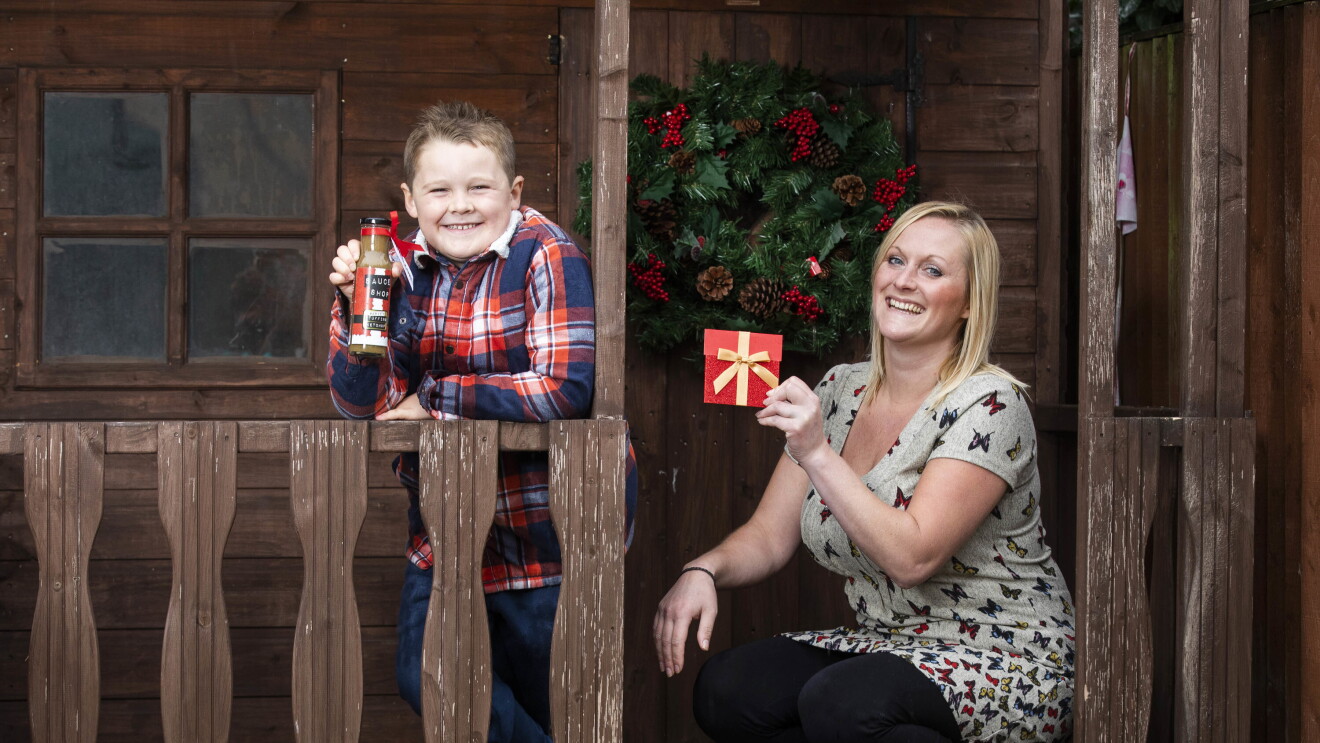 Berty standing on his wooden porch holding his stuffing ketchup bottle next to his mum, who is holding a gift card. 