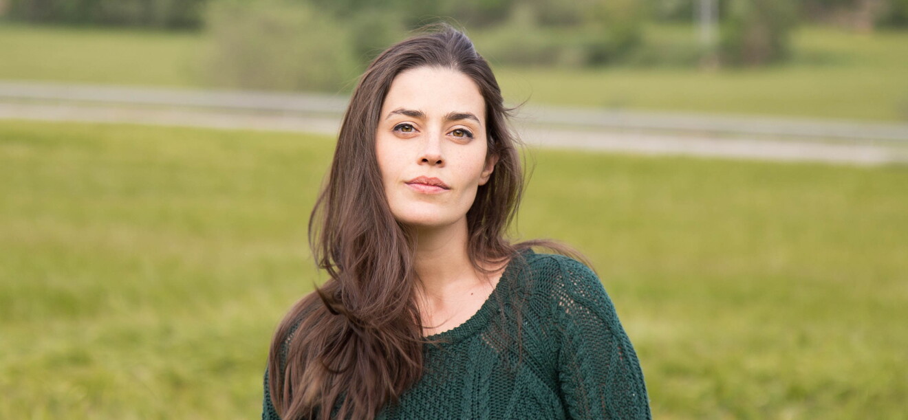 Lorena Franco es escritora y empezó autopublicándose en 2016 con el servicio KDP de Amazon. En un parque con fondo de árboles y césped está un plano corto de Lorena con el pelo castaño y muy largo y al viento. Tiene los ojos marrones azules y mira a cámara sin sonreir. Lleva un jersey de punto calado de color verde. 