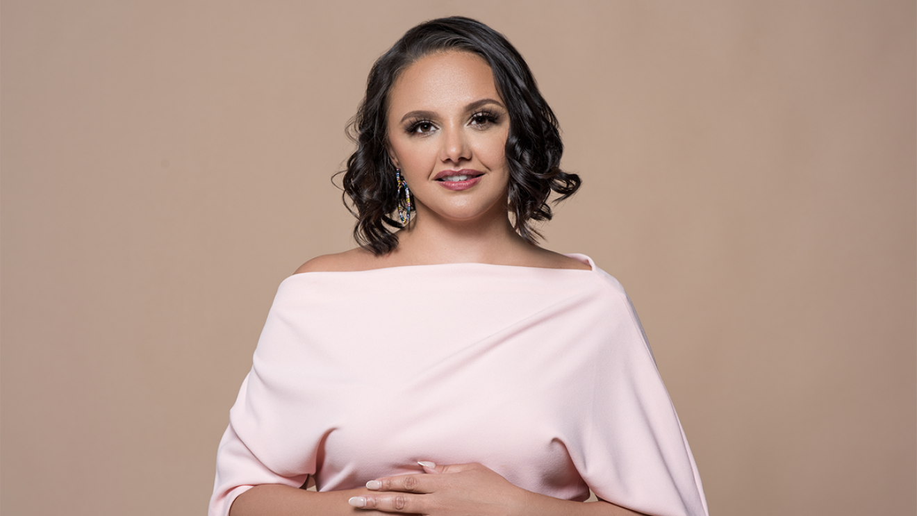 An image of a woman smiling for a photo in front of a light brown background.