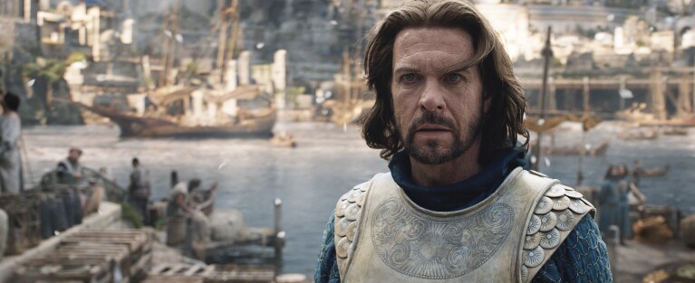 Elendil stares off into the distance toward the camera while walking from the sea.