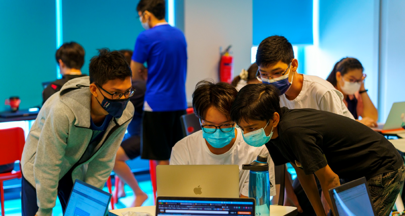 Boys wearing masks huddling over a computer, looking at the screen.