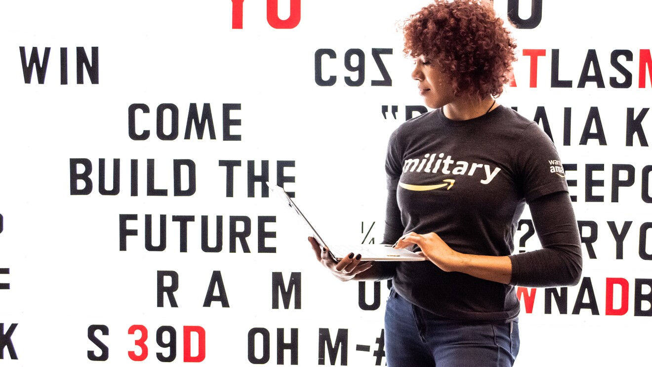 一个女人站在一堵亮着灯的墙前,手里拿着一台笔记本电脑。