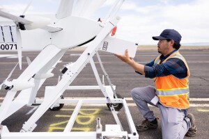 Images of Amazon employees wearing orange safety vests work on drones.