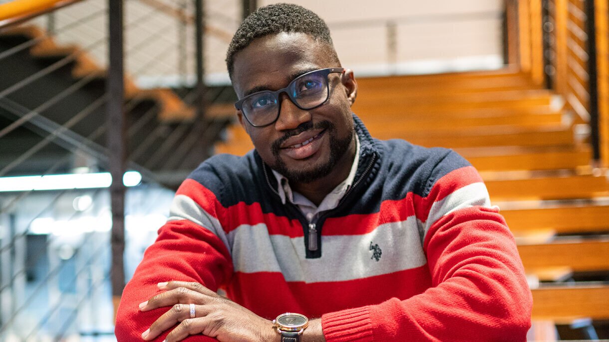 An image of a man sitting on a staircase at an Amazon office smiling for a photo and folding his arms.