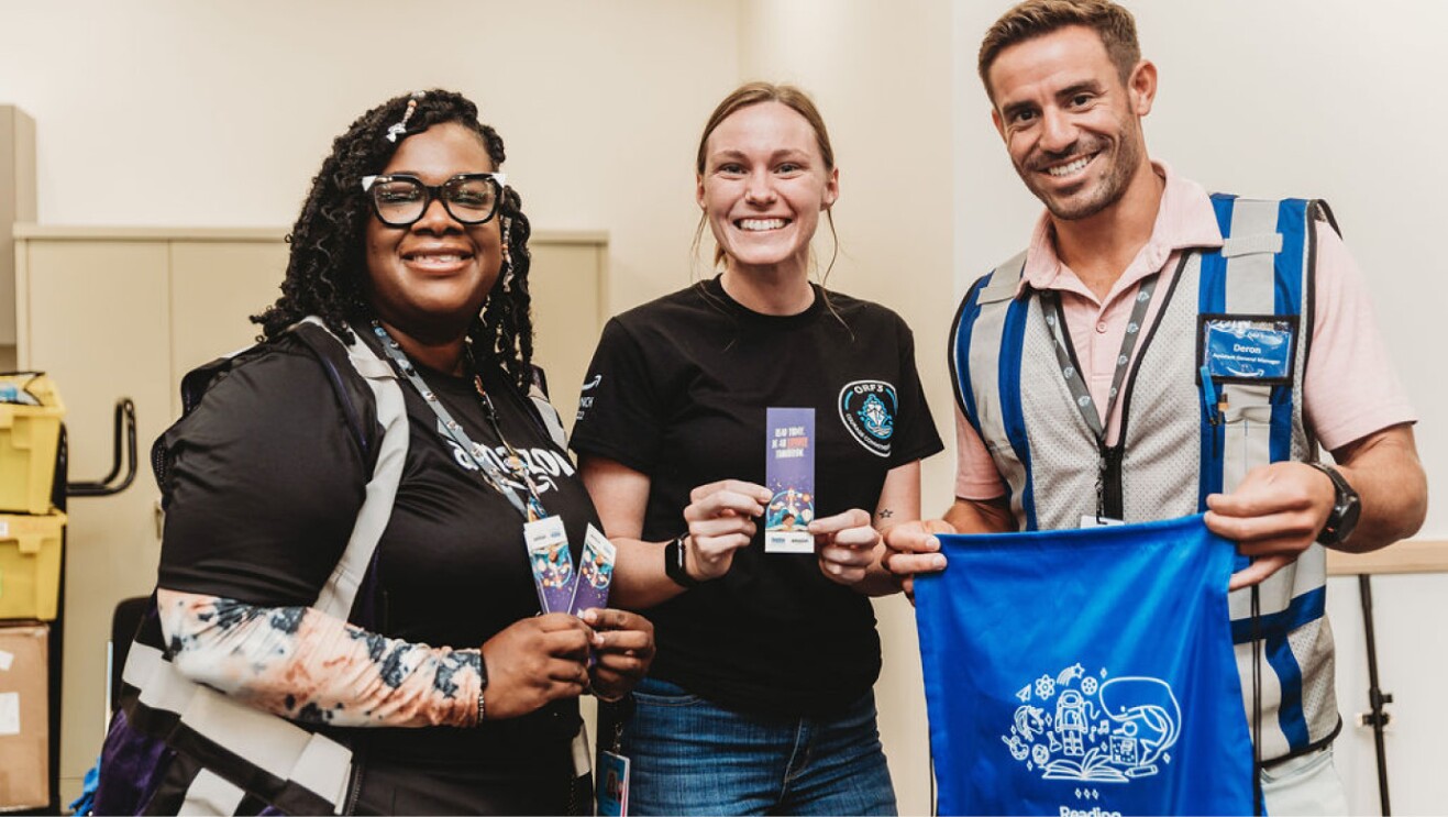 An image of three amazon employees holding up swag while volunteering. 