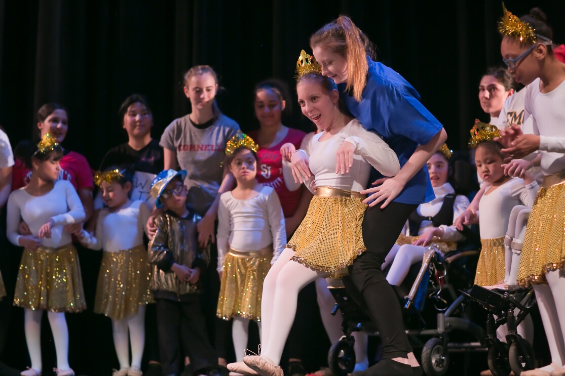 一个舞者穿着芭蕾舞鞋,一枚裙,头饰,白色紧身连衣裤和紧身衣执行。舞蹈家对脑瘫,依靠着一个助手的支持。在后台其他舞者和助手。