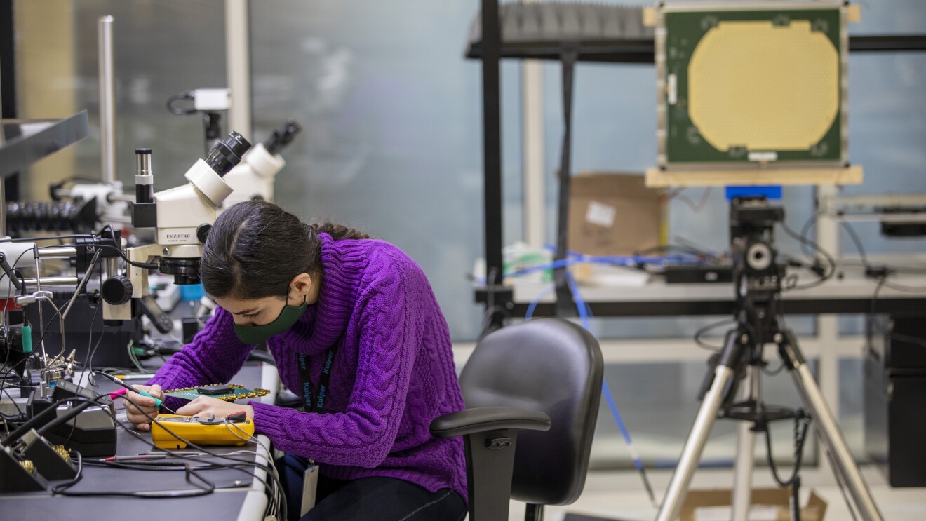 A woman sits at a table while working on an engineering project for Project Kuiper.