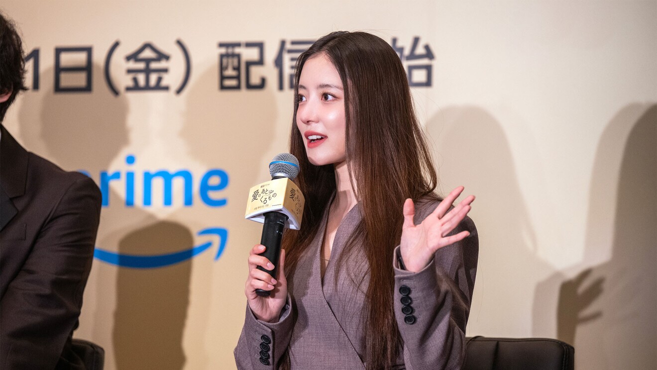 茶色のドレスを着ている女性がマイクを持ち話している。