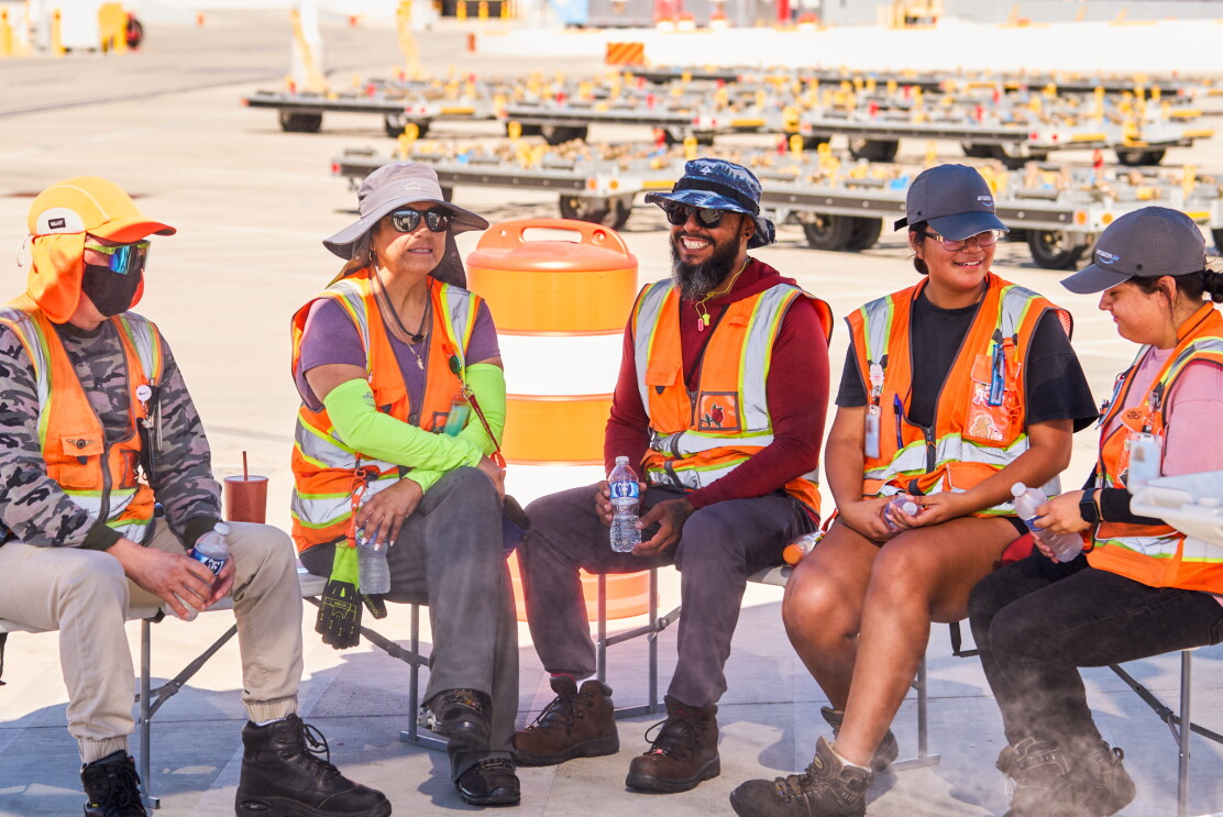 Amazon workers wearing high-visibility vests and sun protection taking a rest break with water bottles