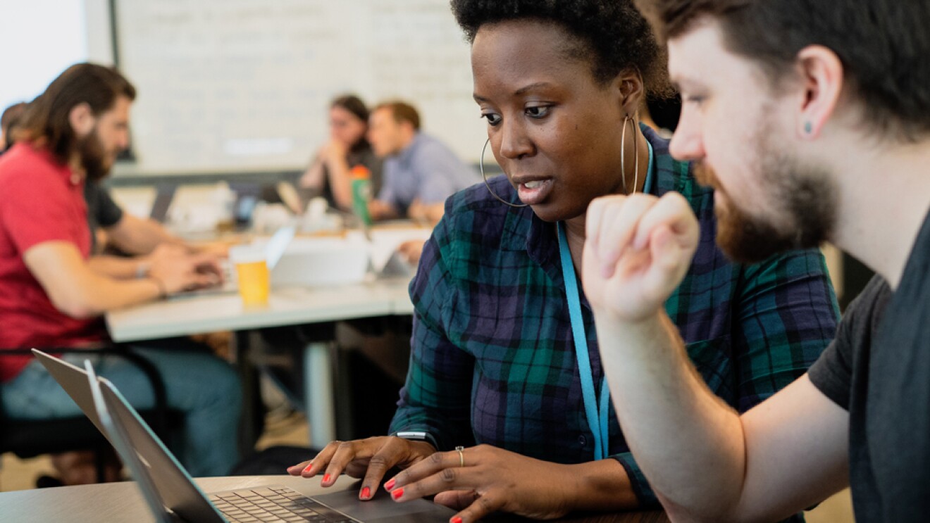 一名男子和一名女子在集体环境中并排使用笔记本电脑工作