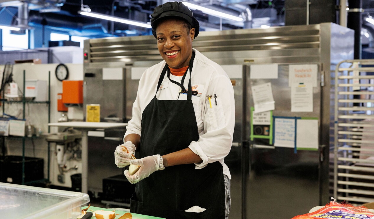 A FareStart team member smiles while preparing food in the kitchen as part of the organization's culinary training program in Seattle.
