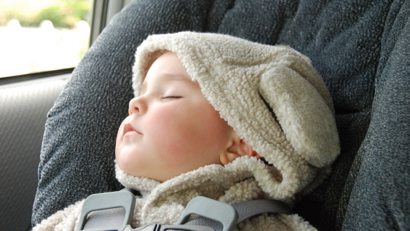 An infant wearing a hooded top with ears has fallen asleep in the carseat