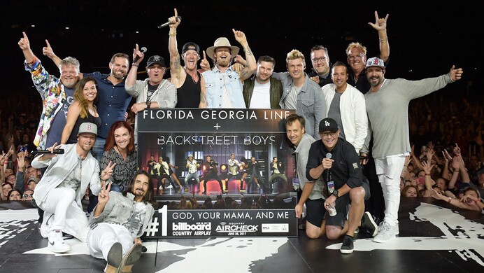 MTK, Florida Georgia Line, and the Backstreet Boys smile for a photo on stage in front of a crowd holding the platinum plaque for the song the two bands wrote together.