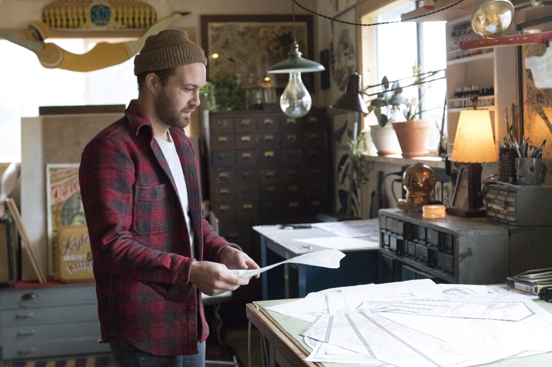 Amazon artist Kyler Martz in his Seattle studio, with a sheaf of drawings on a table.