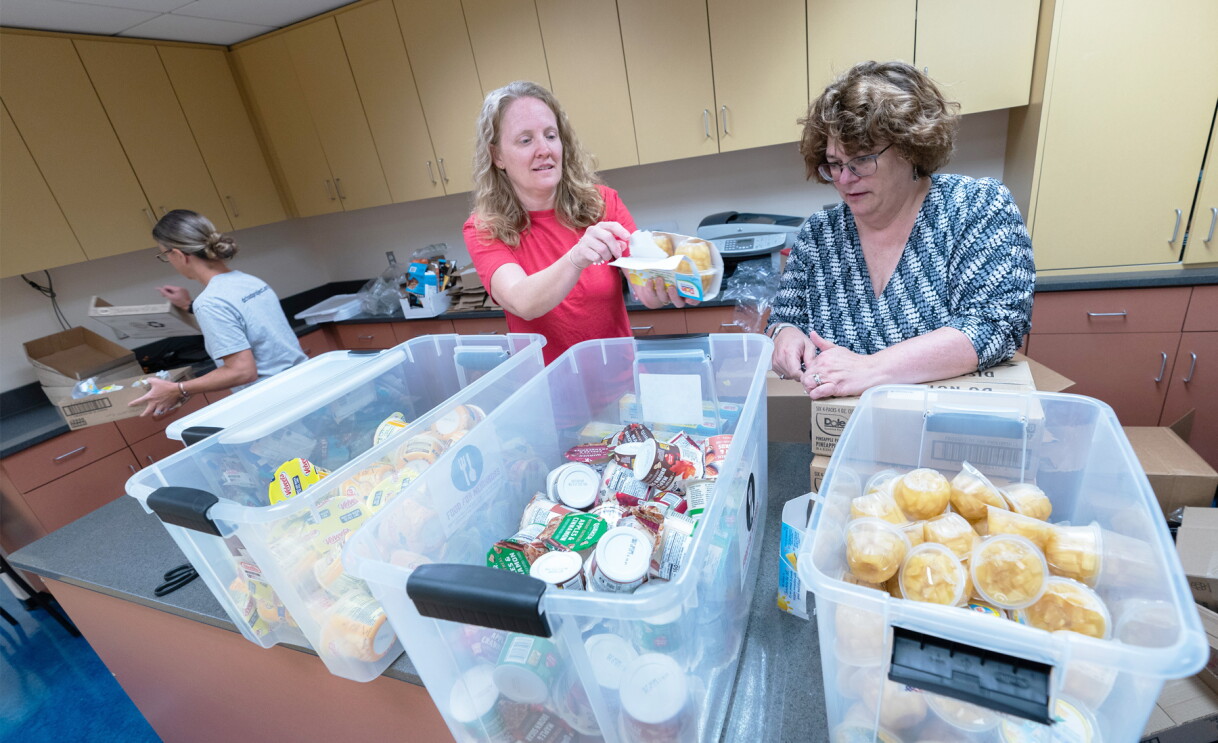 An image of two women sorting food in clear boxes. 