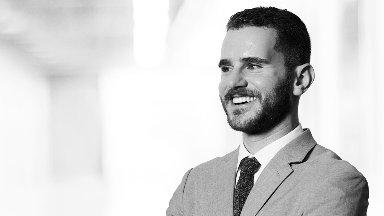 A headshot image of Russell Silver-Fagan. He is standing in a white hallway smiling for the photo.