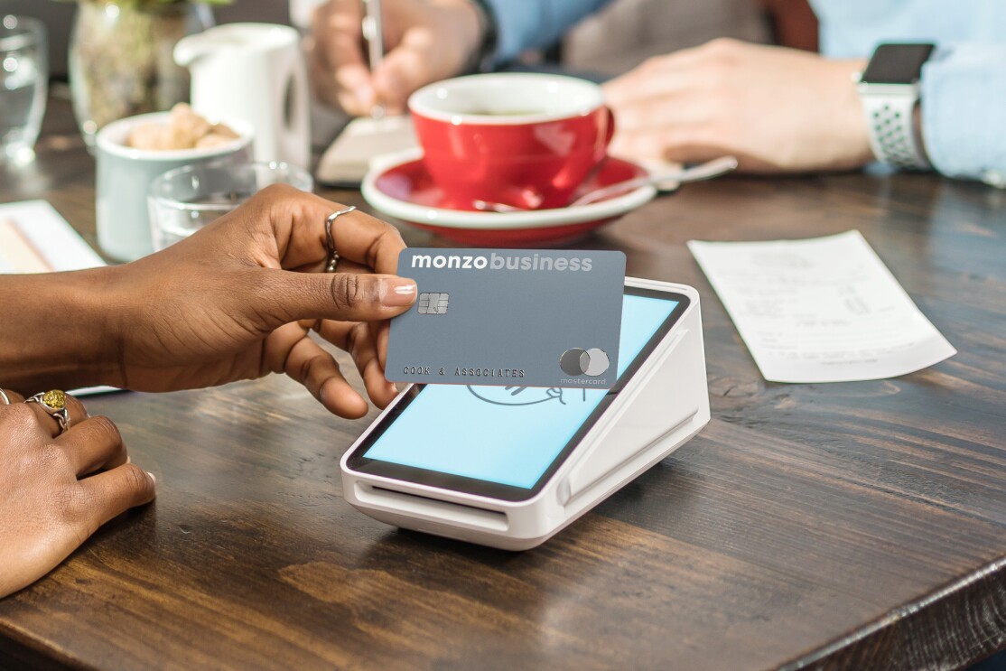 Persons hand with Monzo business card over pay machine 