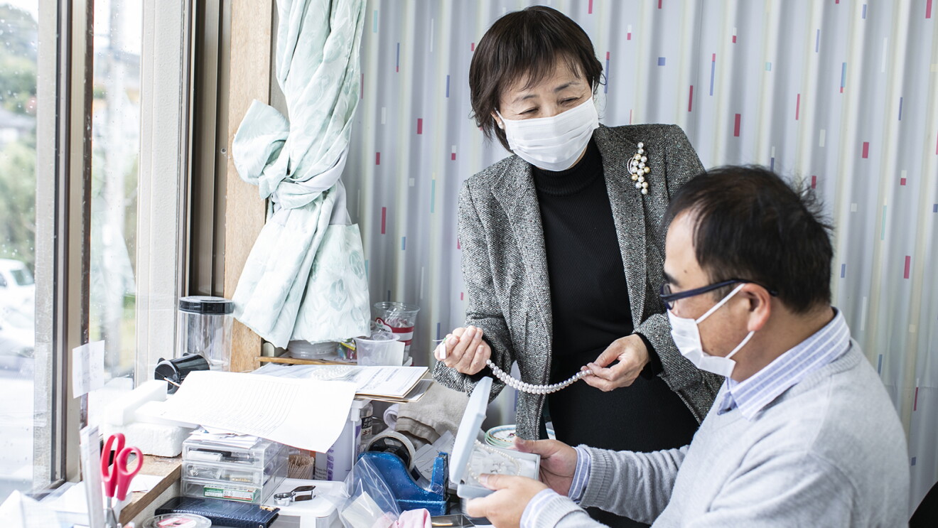 真珠を手に従業員と話をする磯和恵子さん