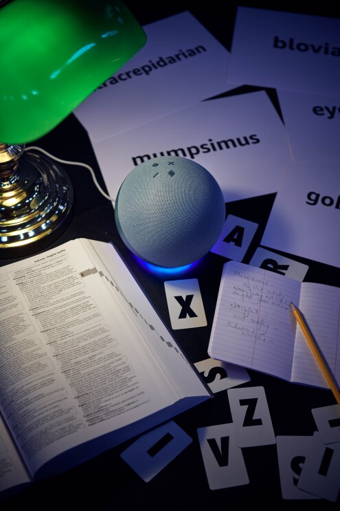 An Amazon Echo on a library table next to a dictionary and a notebook.