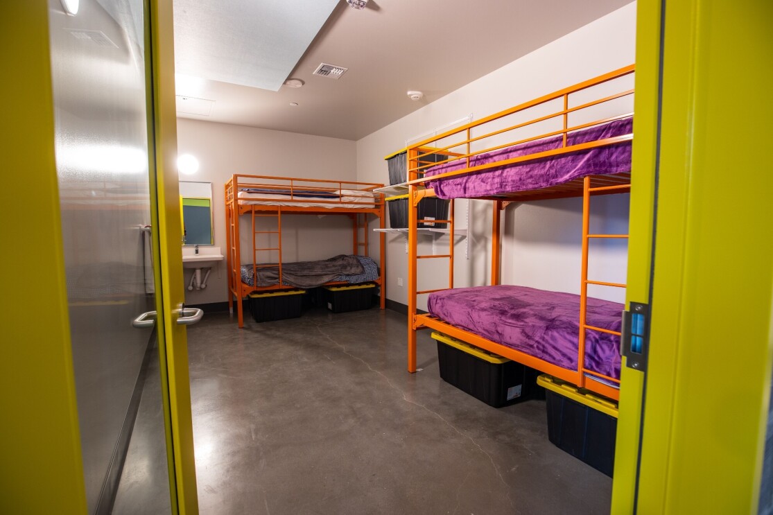 An image looking through a doorway into a room with bunkbeds and a sink.