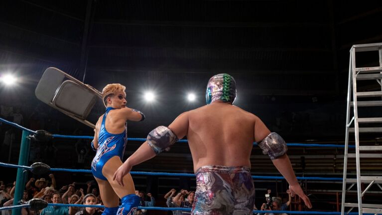 Wrestler swinging chair at masked opponent in wrestling ring.