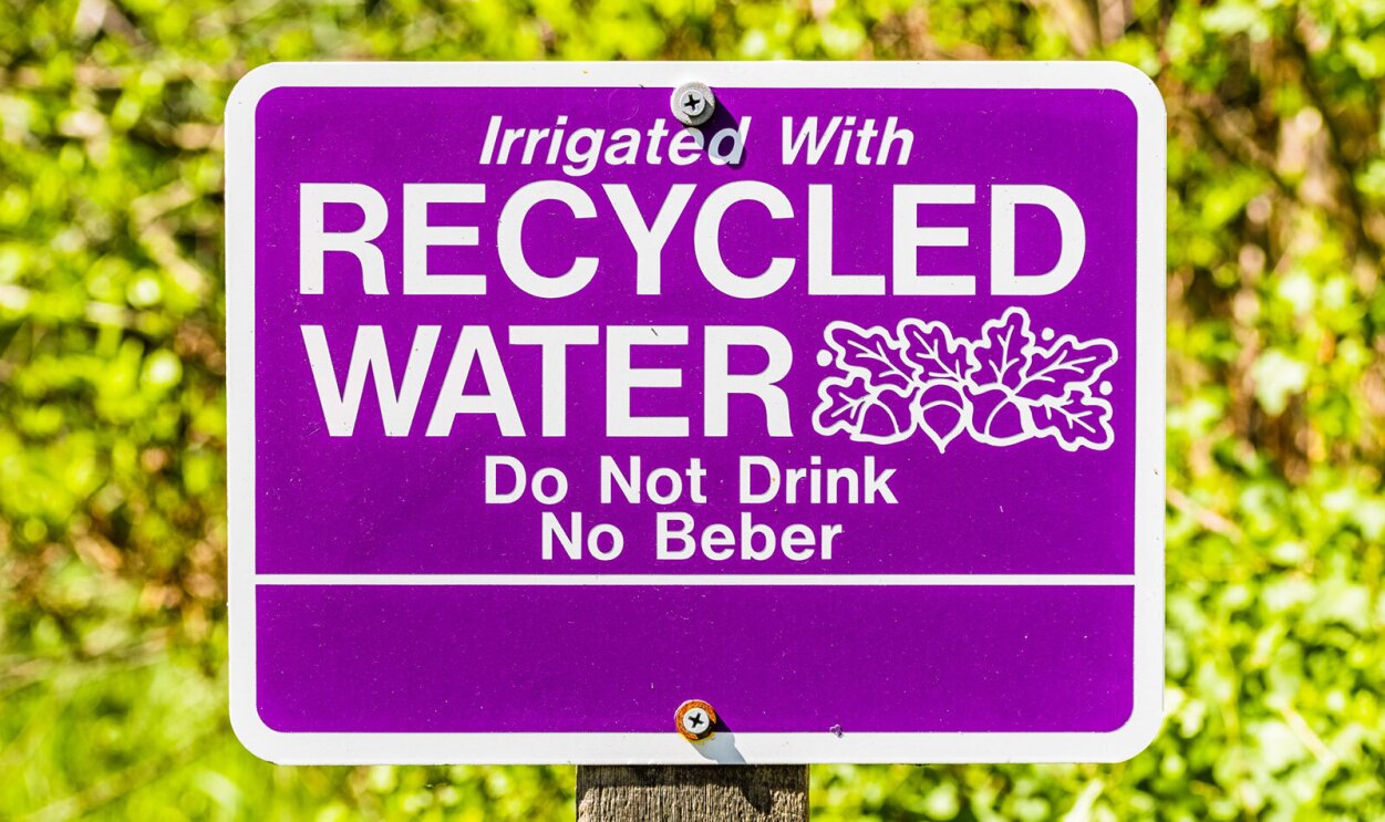 A photo of an outdoor sign that states, "Irrigated with recylcled water, Do Not Drink, No Beber". 