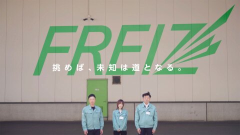 ベージュとグレーの建物の壁面に、緑色で大きく「FREIZ」のロゴ。壁の前に、ライトブルーの作業服を着た3名のスタッフが並んいる。画面中央に白字で「挑めば、未知は道となる。」と横書き。