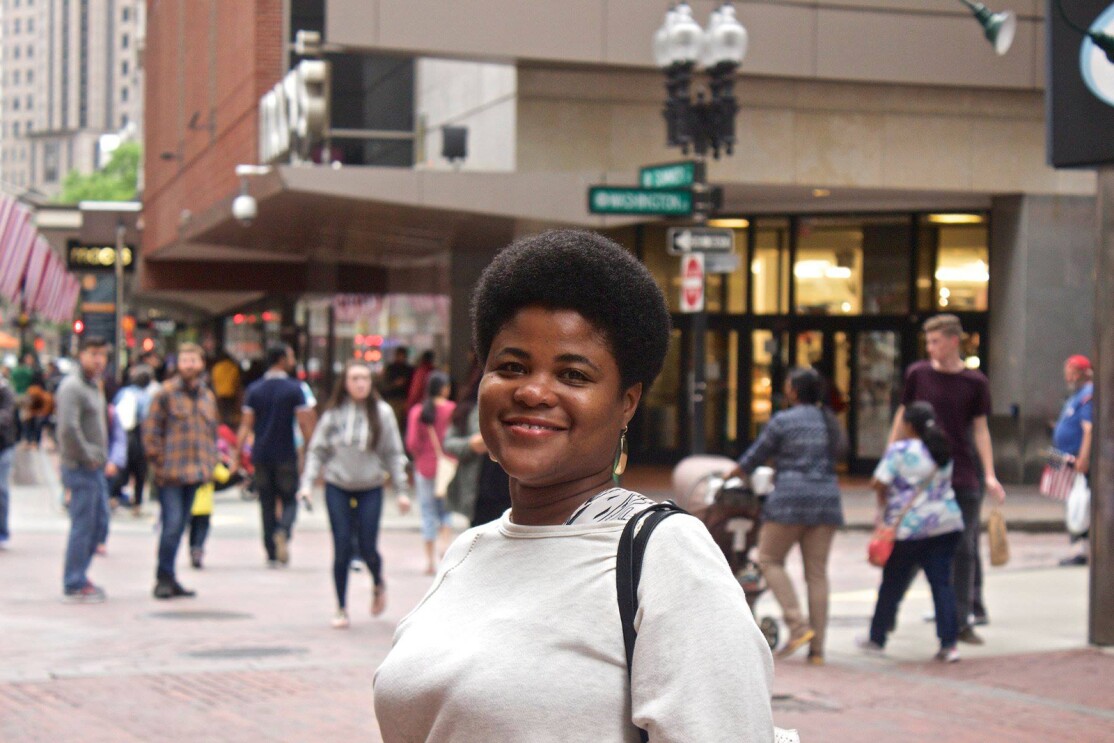 An image of a woman standing in the middle of a sidewalk smiling for a photo. 