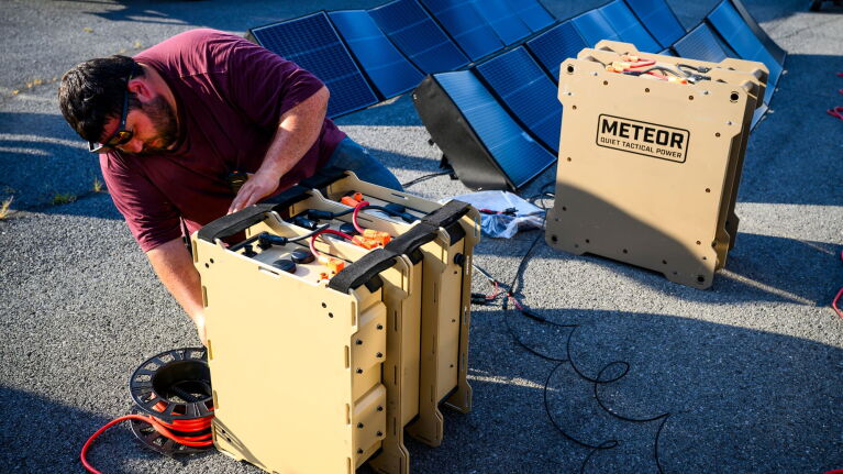 Person configuring Meteor quiet tactical power units connected to solar panels on pavement