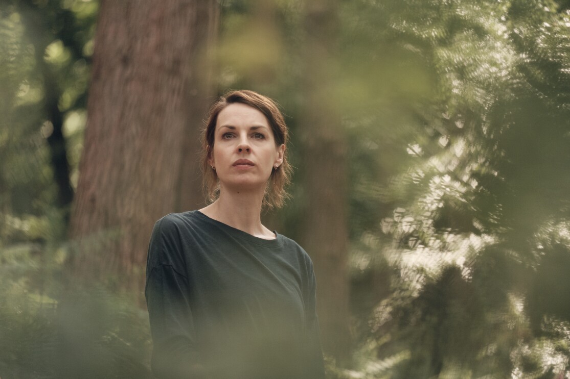A brunette woman looks pensively in a forest