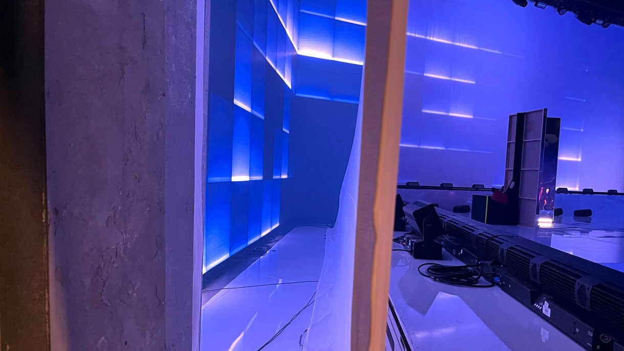 An image showing the digital screen behind the stage set with a layer of white fabric in front of it that allows some of the blue lights to filter through.