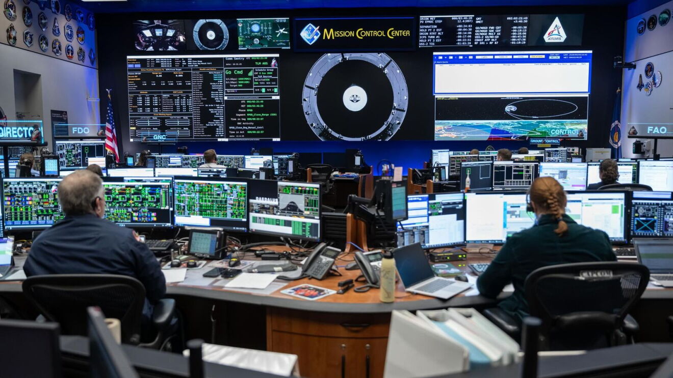 Mission Control Center personnel monitoring multiple screens displaying spacecraft data and tracking information
