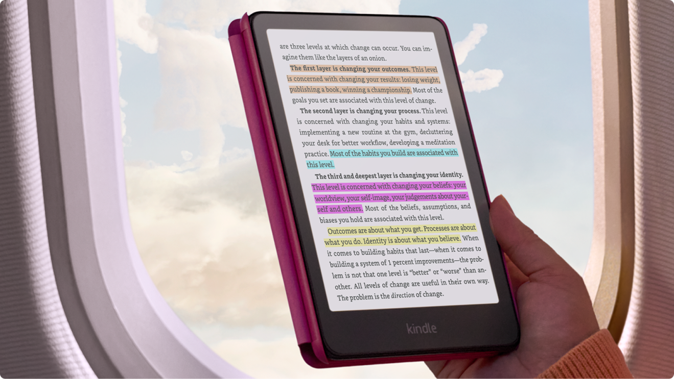A Kindle being held infront of a plane window with clouds outside