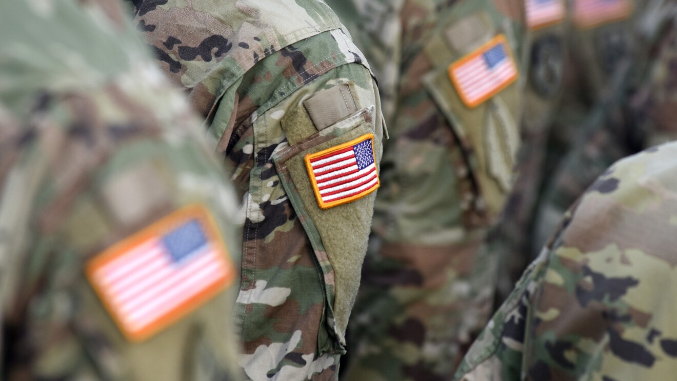 美国士兵站在一起,肩膀上露出美国国旗。他们的脸被遮住了。