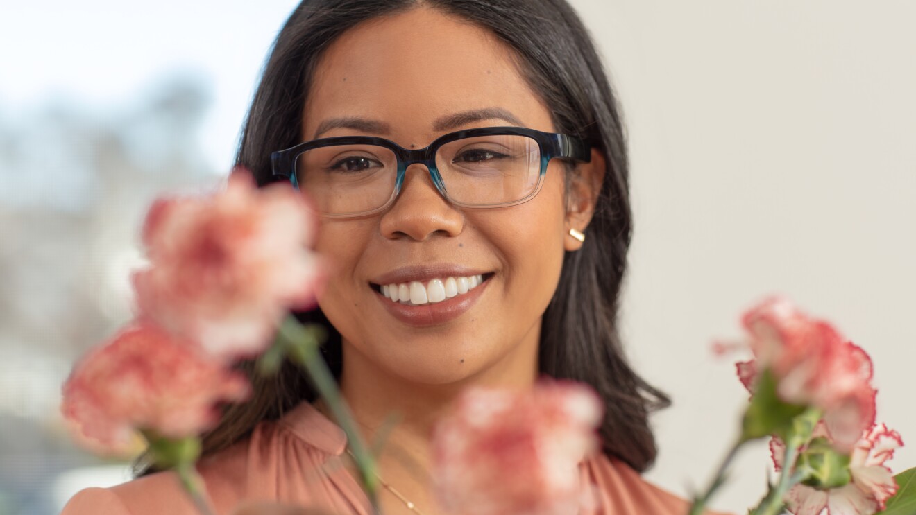 A woman wears Echo Frames in pacific blue and smiles as she looks at flowers.